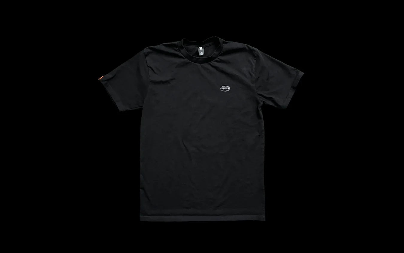 Front of a black t-shirt on black with a small oval logo on the chest