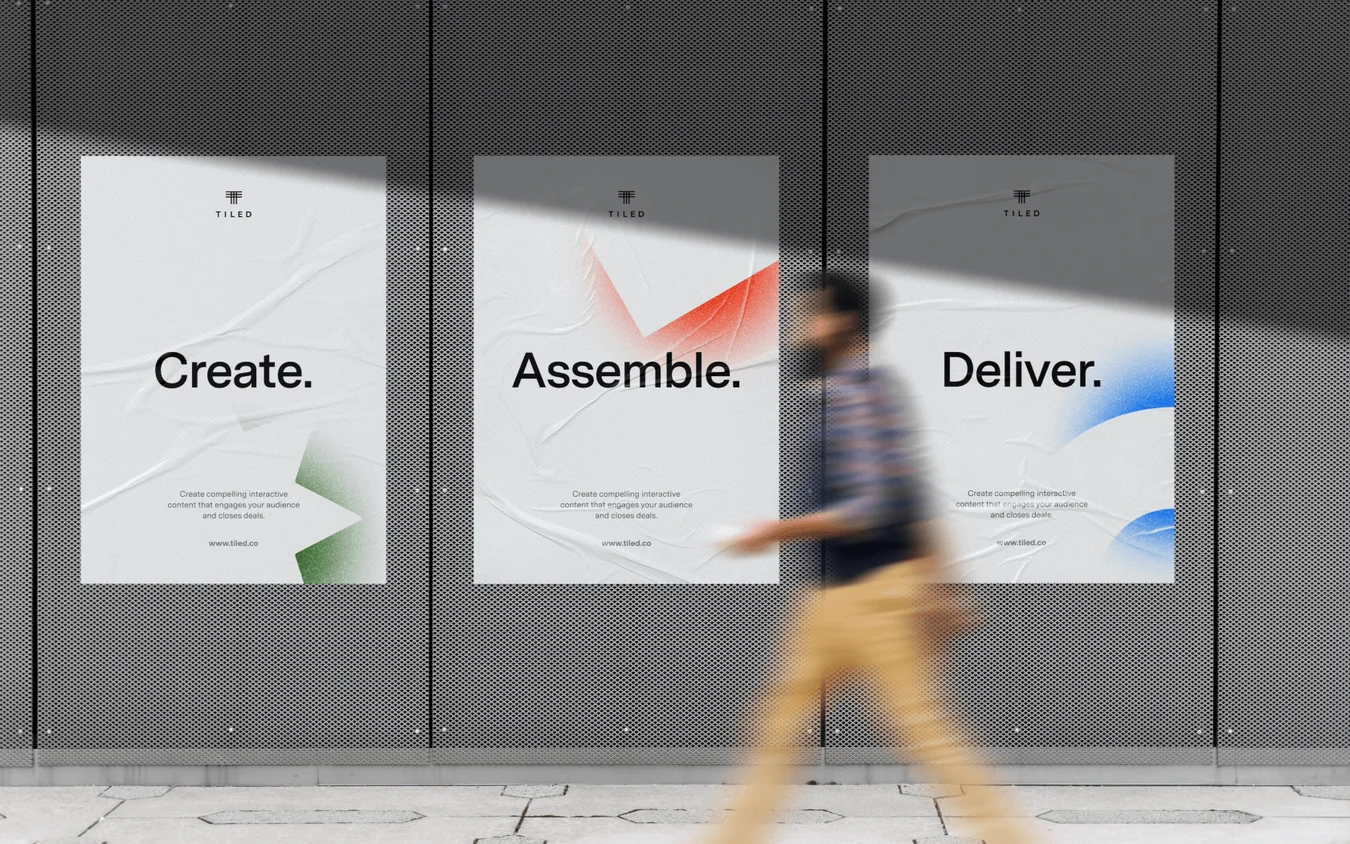 Three posters on a dark grey wall reading Create., Assemble. and Deliver., with a blurred person in yellow trousers walking past