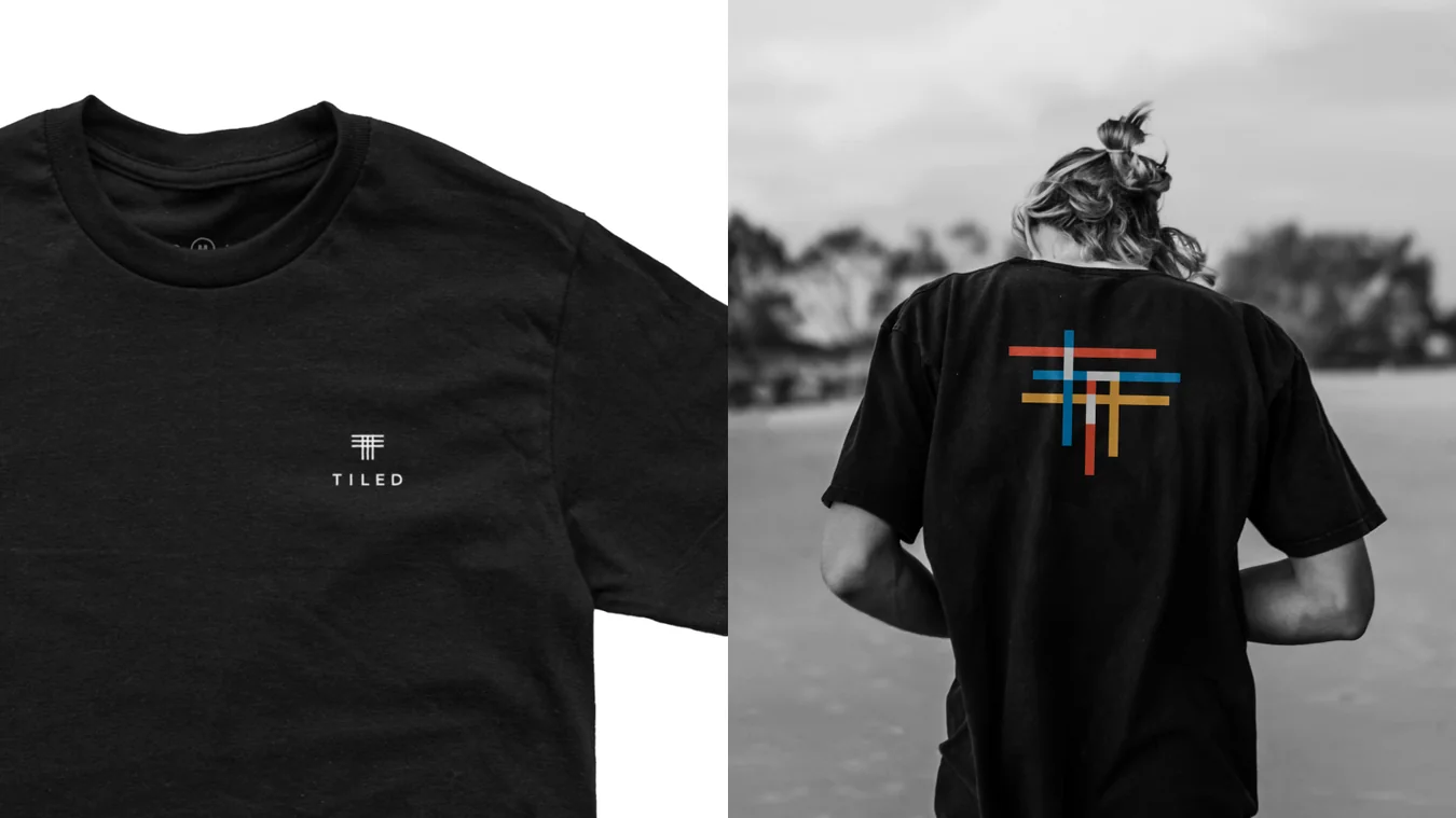 Two photos: a black t-shirt with a small Tiled logo on white, and the back of a black t-shirt with a multicolour crossed-line mark on a person in a grey beach scene