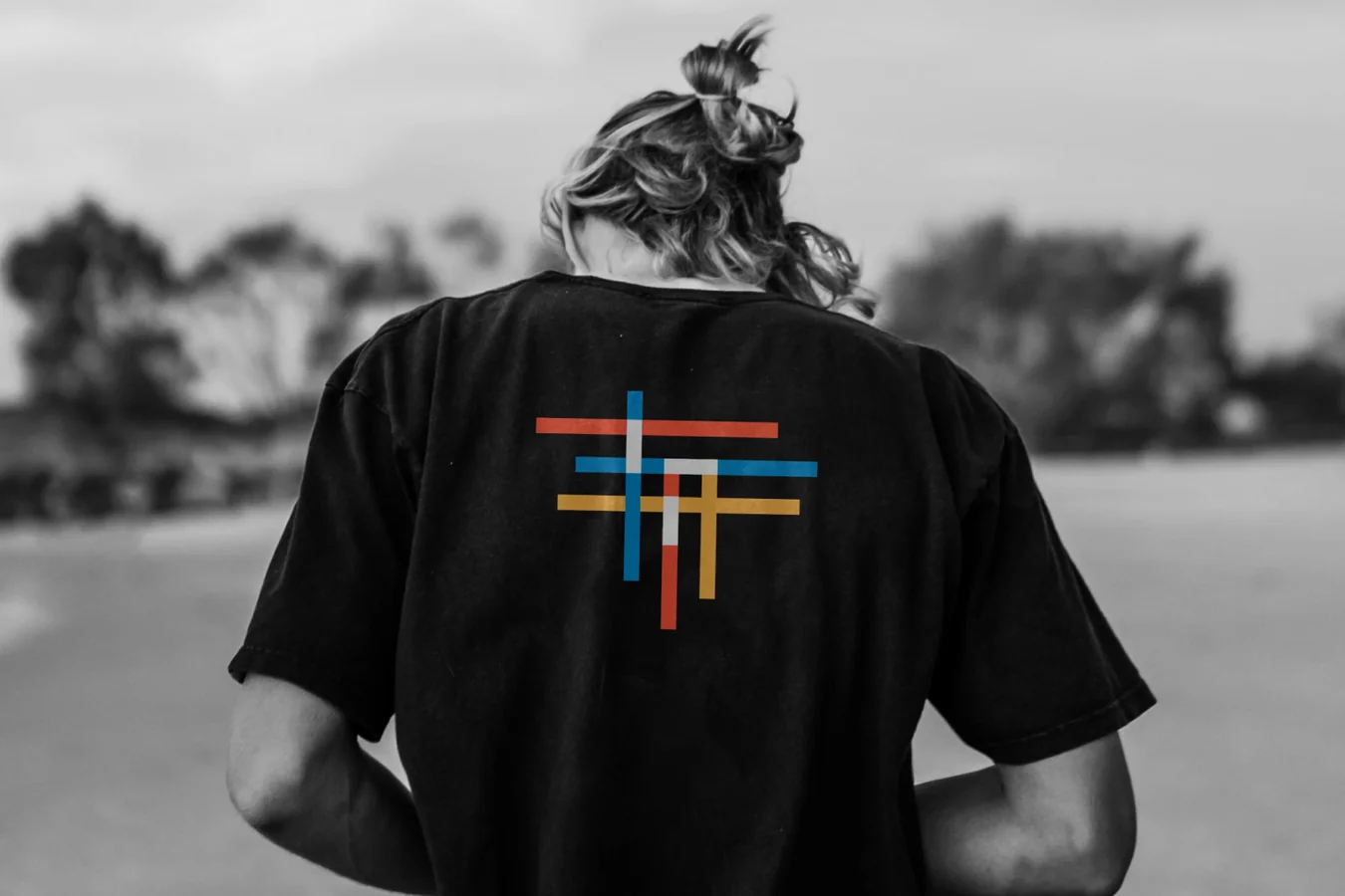 Black and white photo of a person seen from behind in a black t-shirt printed with the Tiled crossed-line mark in red, blue and yellow